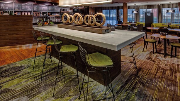 A bar area with a central island, bar stools, and a menu board. - Courtyard by Marriott Alexandria (Alexandria)