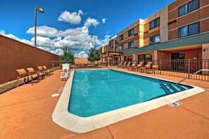 A swimming pool with lounge chairs and umbrellas, surrounded by a building with multiple floors and windows. - Courtyard by Marriott Alexandria (Alexandria)
