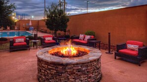 A stone fire pit surrounded by wicker chairs with red cushions, a pool, and a cloudy sky. - Courtyard by Marriott Alexandria (Alexandria)