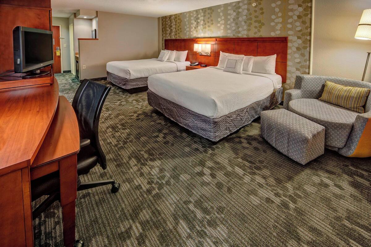 A hotel room with two beds, a desk with a TV, a chair, and a lamp.