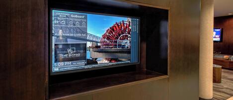 A digital display in a hotel lobby with a large screen showing a weather forecast, a restaurant menu, and a timestamp.
