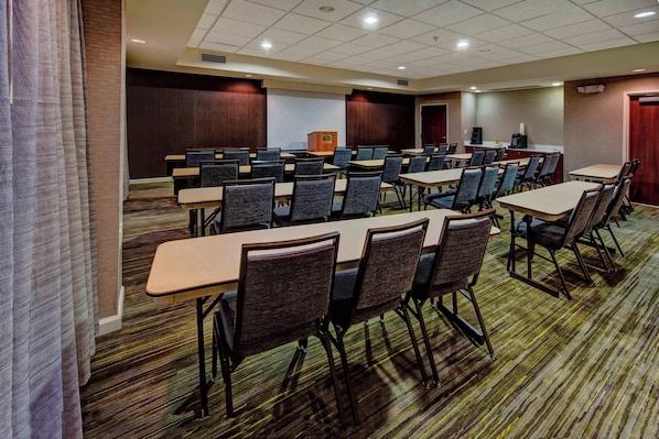 A conference room with multiple tables and chairs, a podium, and a carpeted floor.
