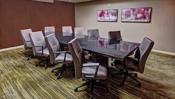 A conference room with a large table and chairs, carpeted floor, and two framed pictures on the wall.