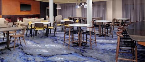 Un hall d’hôtel doté de plusieurs espaces de détente, comprenant des tables et des chaises rondes, ainsi qu’un grand téléviseur à écran plat fixé au mur.