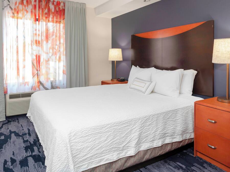 A hotel room with a large bed, two bedside tables, a headboard, and a window with curtains.