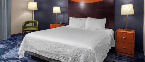 A hotel room with a large bed, two nightstands with lamps, a green chair, and a dark blue carpet.