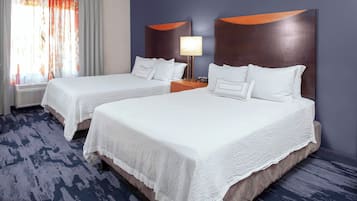 A hotel room with two beds, a nightstand with a lamp, and a window with curtains.