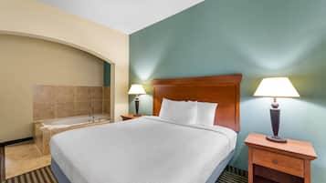 A hotel room with a large bed, two bedside lamps, a wooden nightstand, a bathroom with a bathtub, and a green accent wall.
