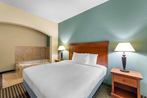 A hotel room with a large bed, two bedside lamps, a wooden nightstand, a bathroom with a bathtub, and a green accent wall.