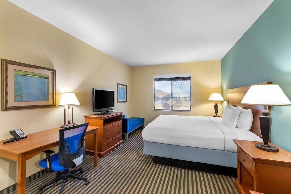 Habitación de hotel con cama, escritorio, silla, televisor y dos lámparas.