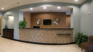 A reception area with a stone counter, a flat-screen TV, decorative mirrors, and potted plants. - Quality Inn & Suites - Marlin (Marlin)