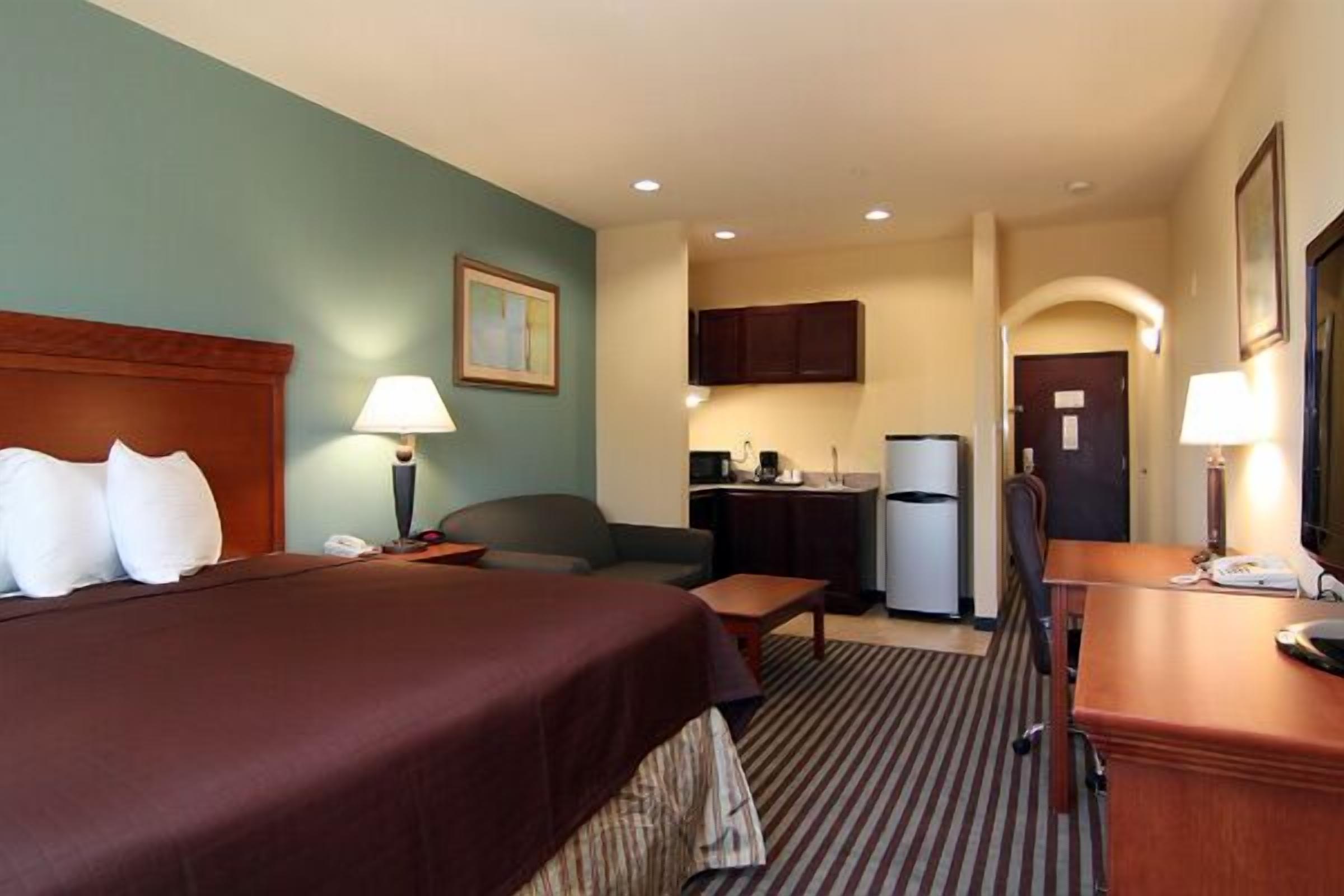A hotel room with a bed, a desk, a chair, a small table, a refrigerator, and a microwave.
