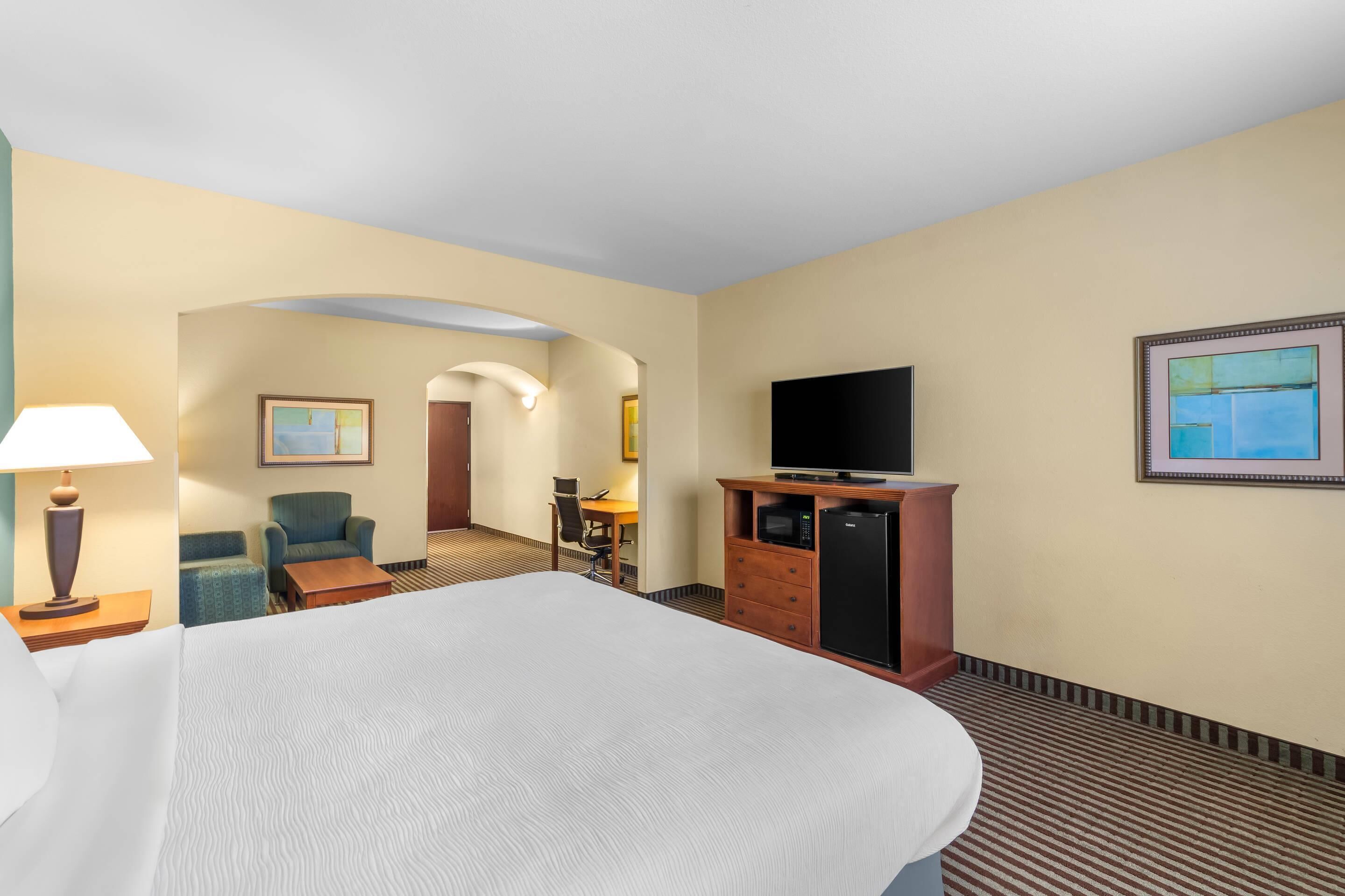 A hotel room with a large bed, a desk with a chair, a television on a wooden cabinet, and a microwave.