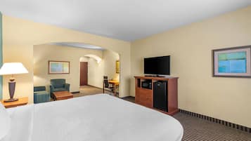 A hotel room with a large bed, a desk with a chair, a television on a wooden cabinet, and a microwave.