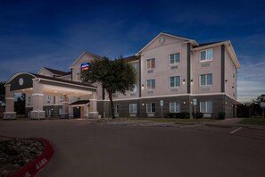 A multi-story hotel with a gas station on the ground floor, featuring a large parking lot and a well-lit entrance.
