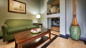 A living room with a green patterned sofa, a wooden coffee table with a floral centerpiece, a large decorative vase, and a framed artwork on the wall. - Quality Inn & Suites - Marlin (Marlin)