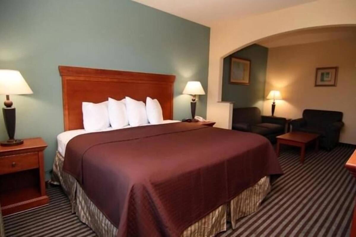 Una habitación de hotel con una cama grande, dos mesitas de noche con lámparas, una silla y una pequeña mesa.