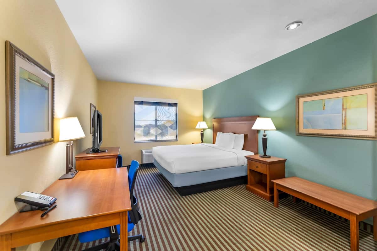 Habitación de hotel con cama, escritorio, silla y dos mesitas de noche con lámparas.