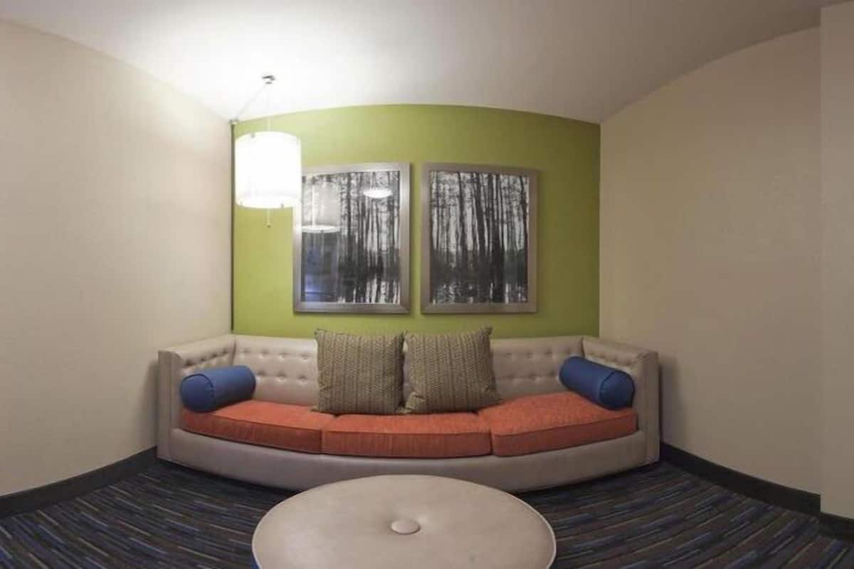 A corner room with a curved sofa, two framed pictures on the wall, and a round ottoman.