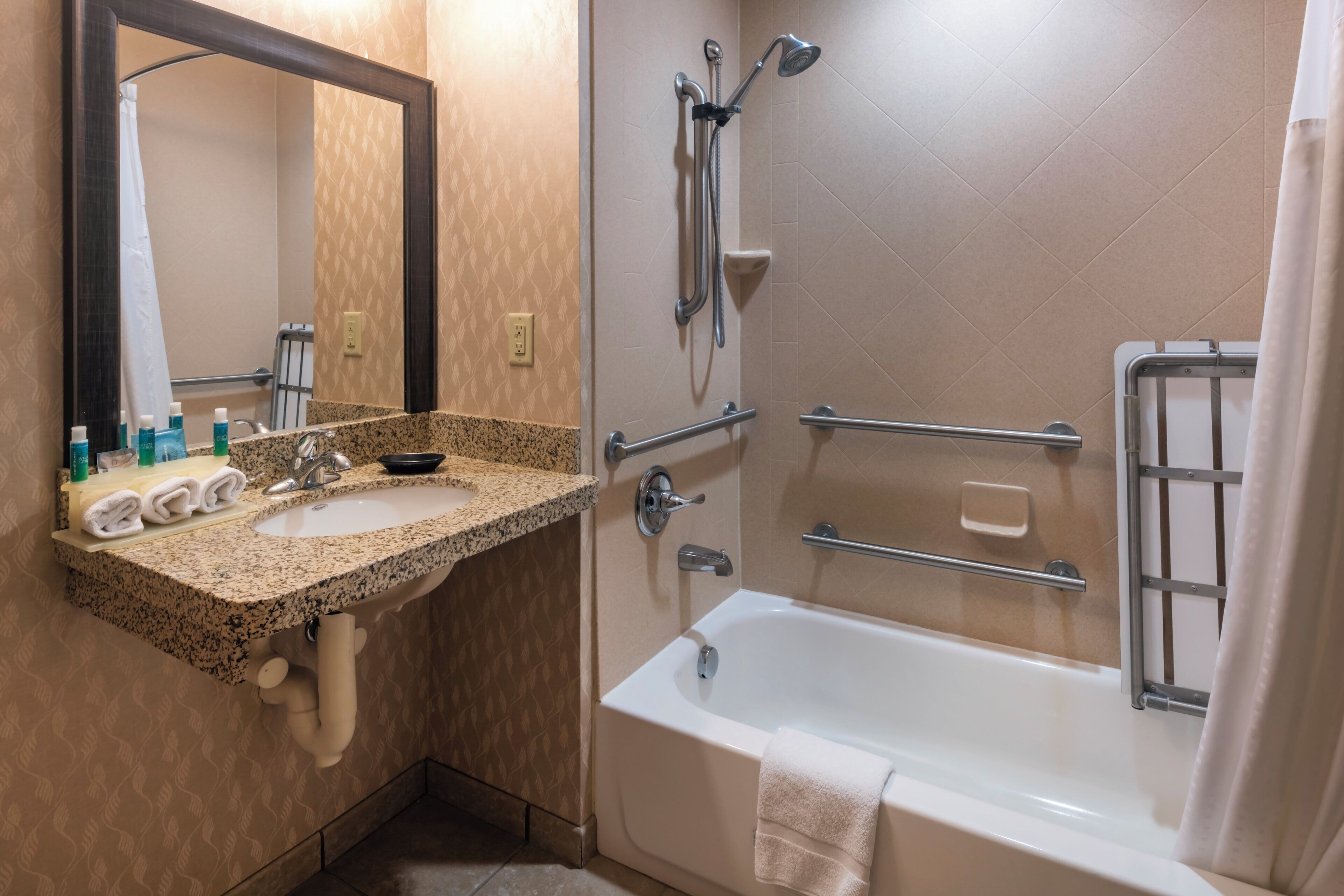 Baño con lavamanos de encimera de granito, espejo, bañera con ducha y barandilla.