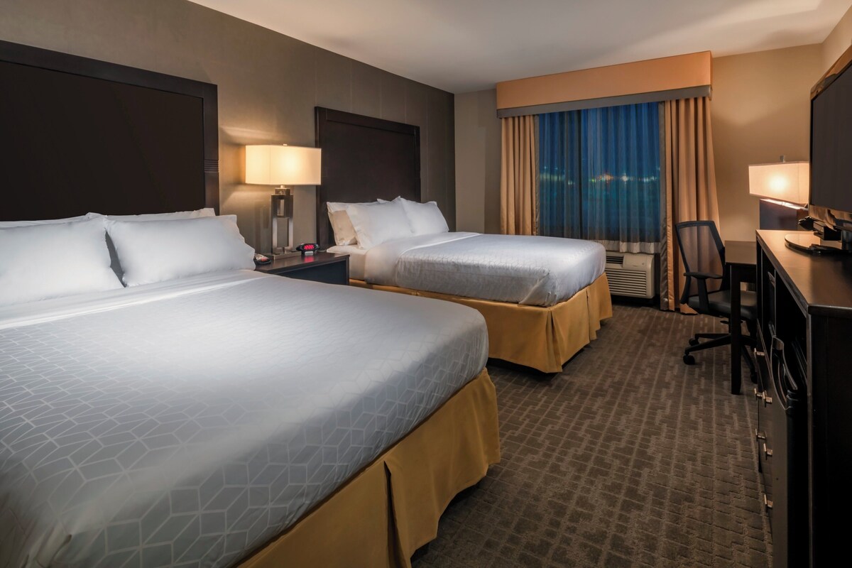 A hotel room with two beds, a desk, a chair, a TV, and a window with curtains.