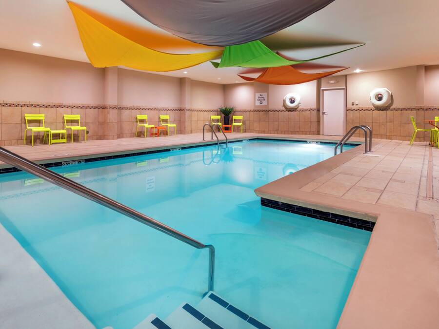 Una piscina con agua cristalina azul, rodeada de sillas amarillas, y un letrero que indica que no se permite bucear en la pared.