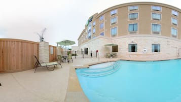 A hotel with a swimming pool, outdoor seating, and a stone facade.