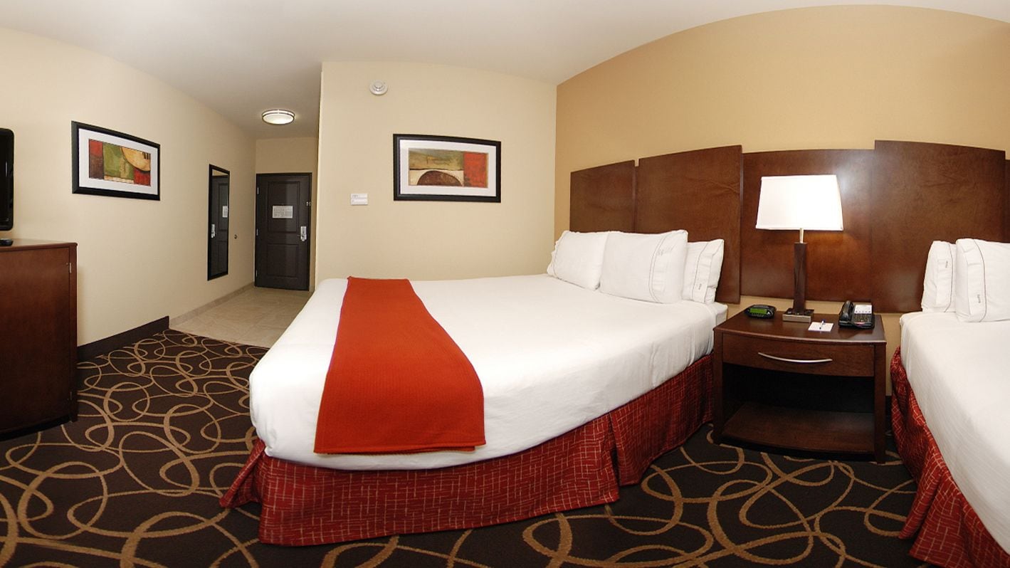 A hotel room with a large bed, a bedside table with a lamp, and a door leading to a hallway.