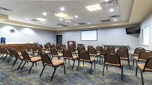 A conference room with rows of chairs, a projector screen, a coffee machine, and a presentation podium. - Holiday Inn Express & Suites Houston South - Pearland by IHG (Houston)