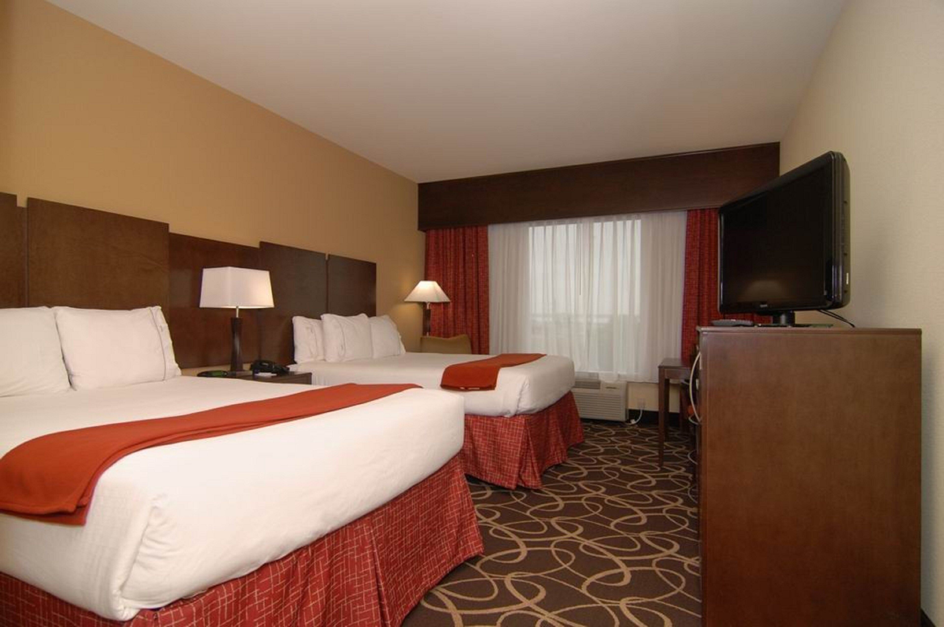 A hotel room with two beds, a television, a desk, and a window with curtains.