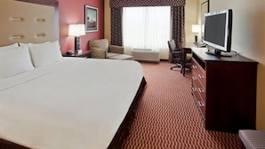 Une chambre d’hôtel avec un grand lit, un bureau avec une télévision, une chaise et une fenêtre avec des rideaux.