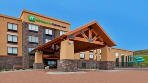 A Holiday Inn Express & Suites building with a stone facade, large entrance canopy, and a blue water slide in the background. - Holiday Inn Express Hotel & Suites Great Falls by IHG (Great Falls)