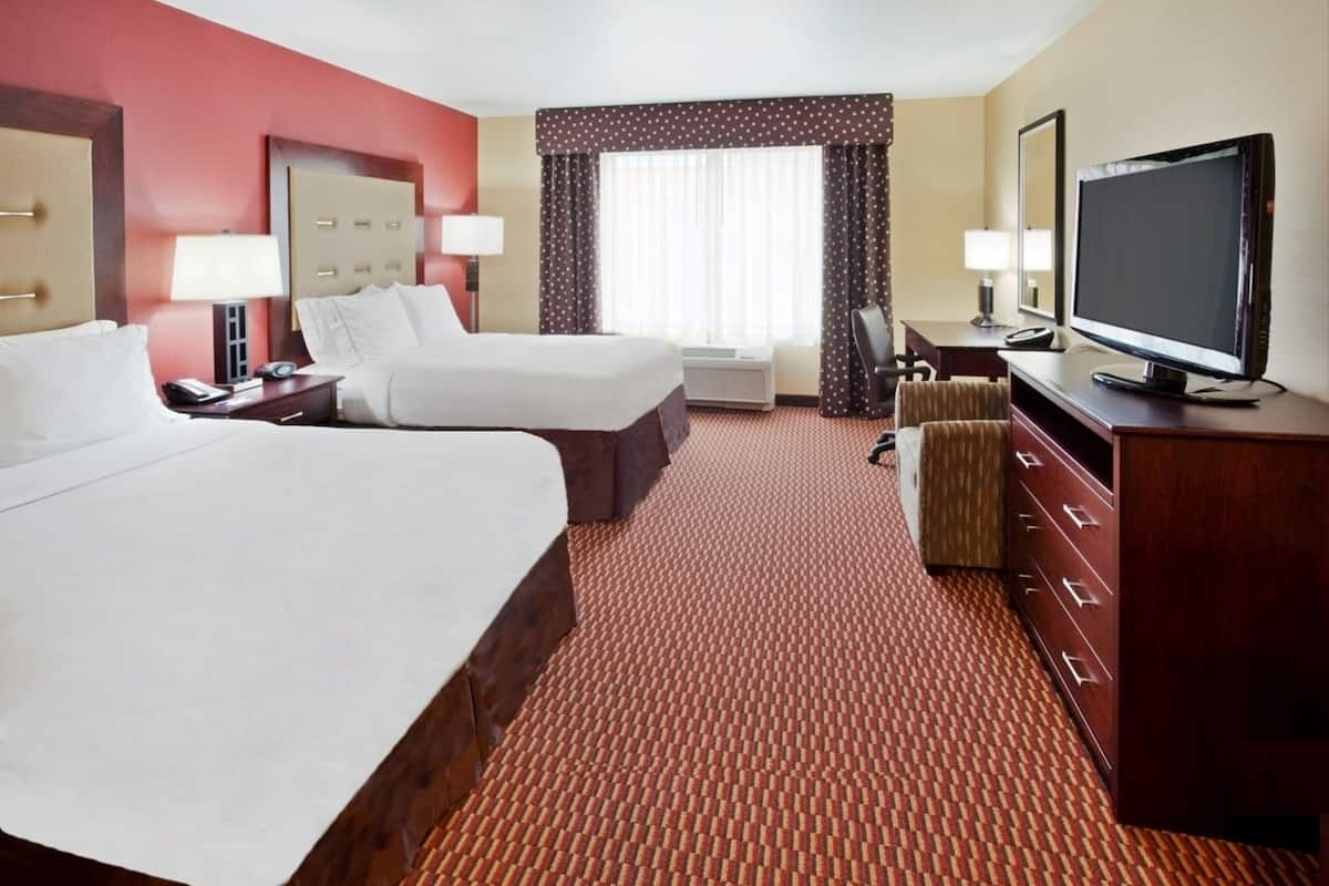 A hotel room with two beds, a TV, a desk, and a chair.