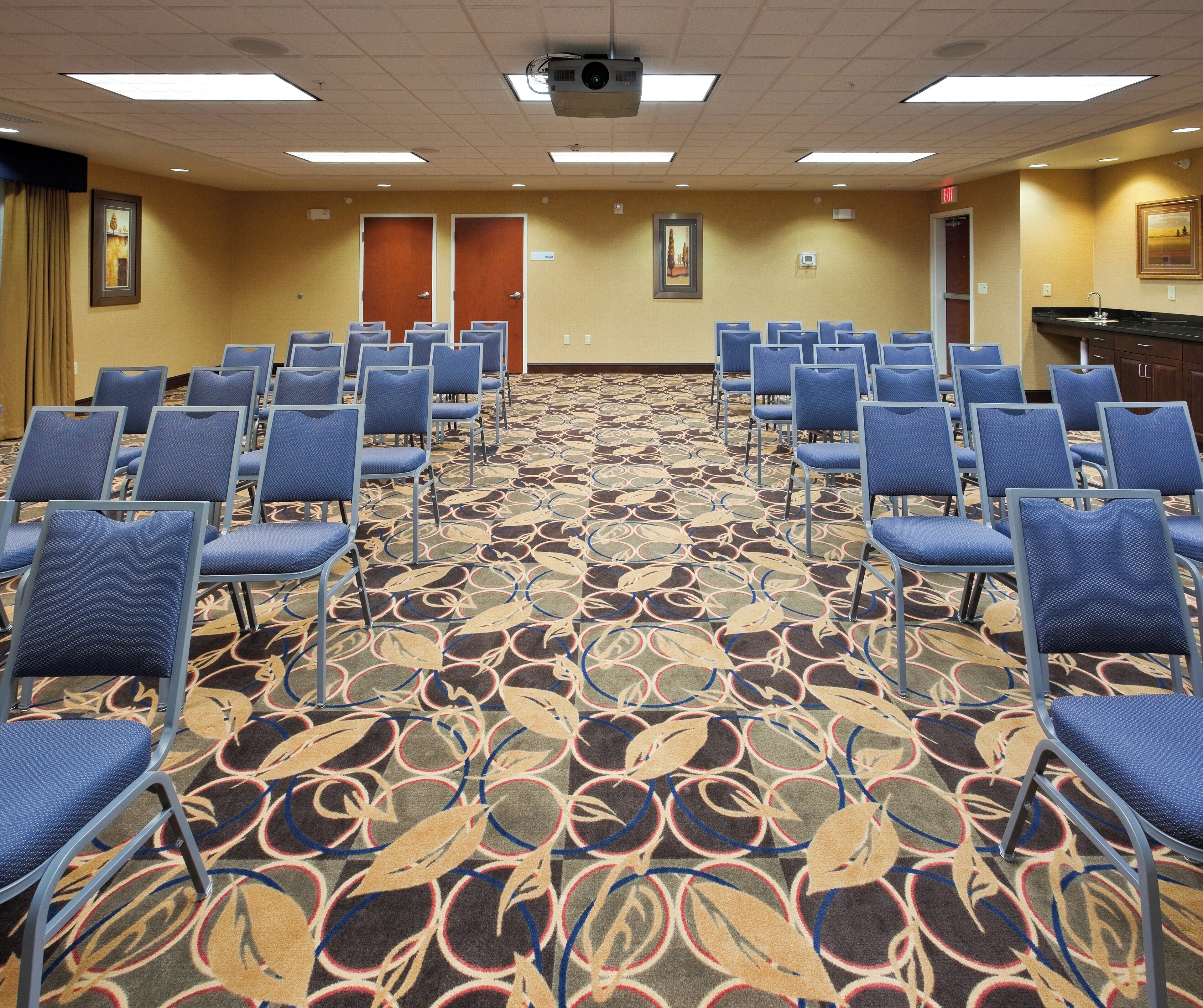 A conference room with rows of chairs, a carpeted floor, and a projector on the ceiling.