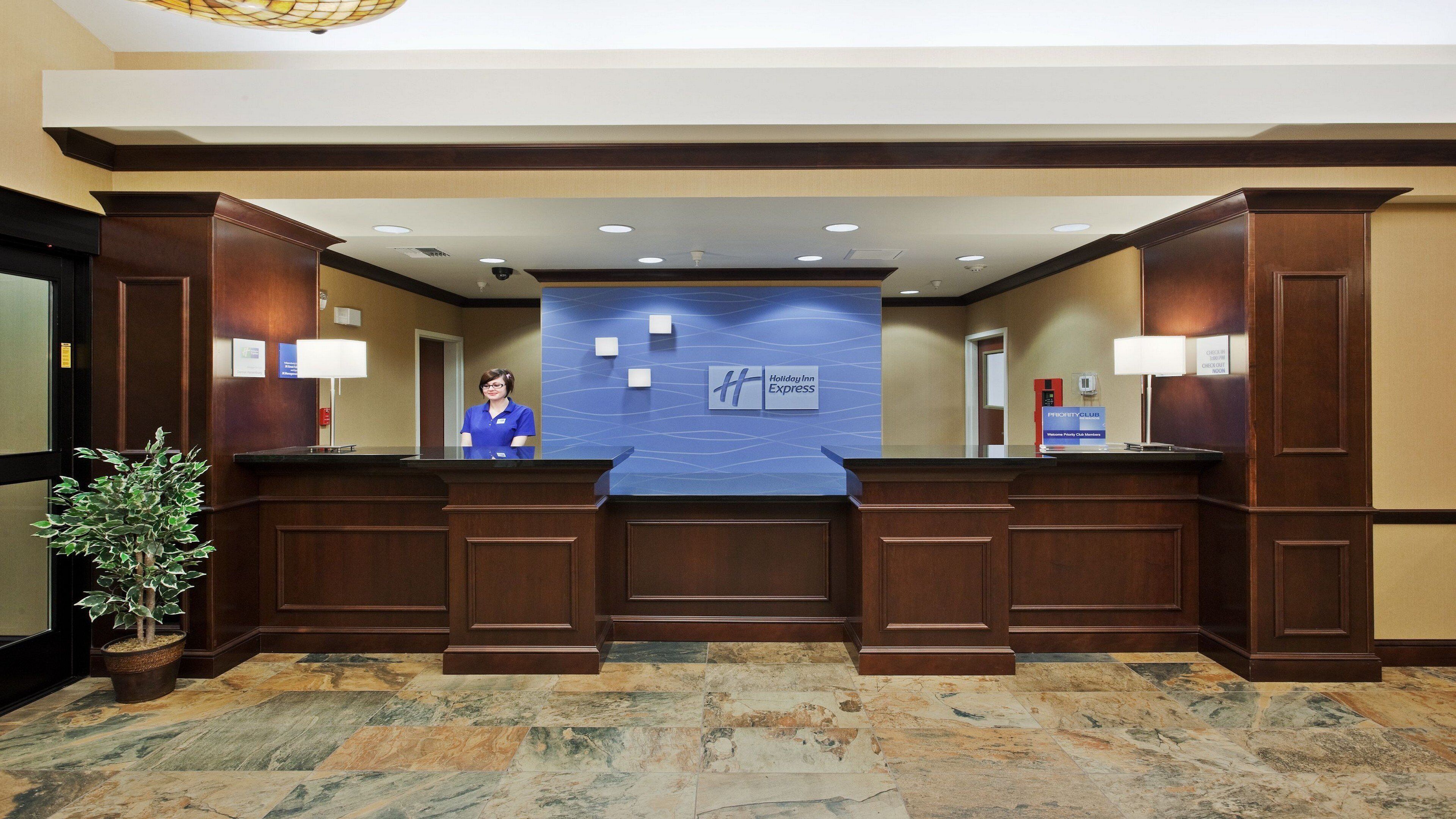 A hotel reception area with a receptionist, a Holiday Inn Express sign, a Priority Club sign, and a reception desk.