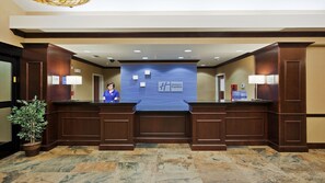 A hotel reception area with a receptionist, a Holiday Inn Express sign, a Priority Club sign, and a reception desk. - Holiday Inn Express Hotel & Suites Great Falls by IHG (Great Falls)