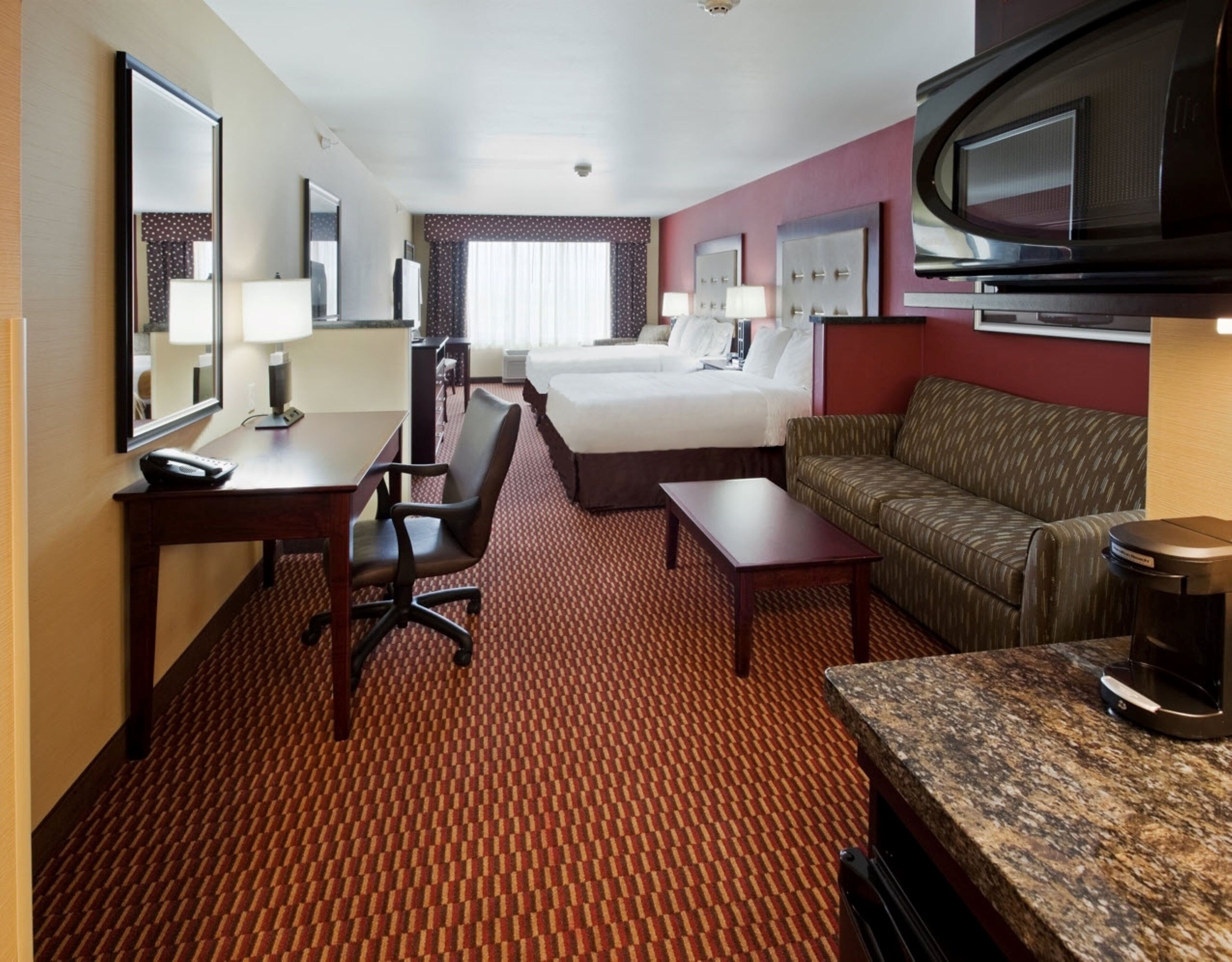 A hotel room with a bed, a desk, a chair, a sofa, a television, and a coffee maker.