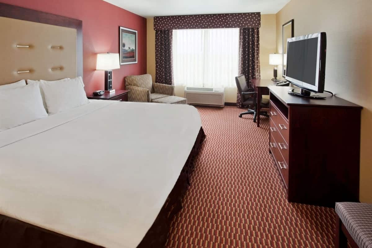 A hotel room with a large bed, a desk with a television, a chair, and a window with curtains.