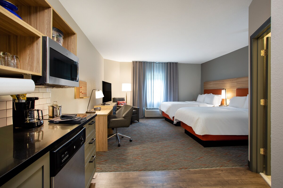 A hotel room with a kitchenette, a bed, a desk, and a television.