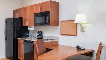 A compact kitchen with wooden cabinets, a black refrigerator, a microwave, a coffee maker, and a table with a chair.