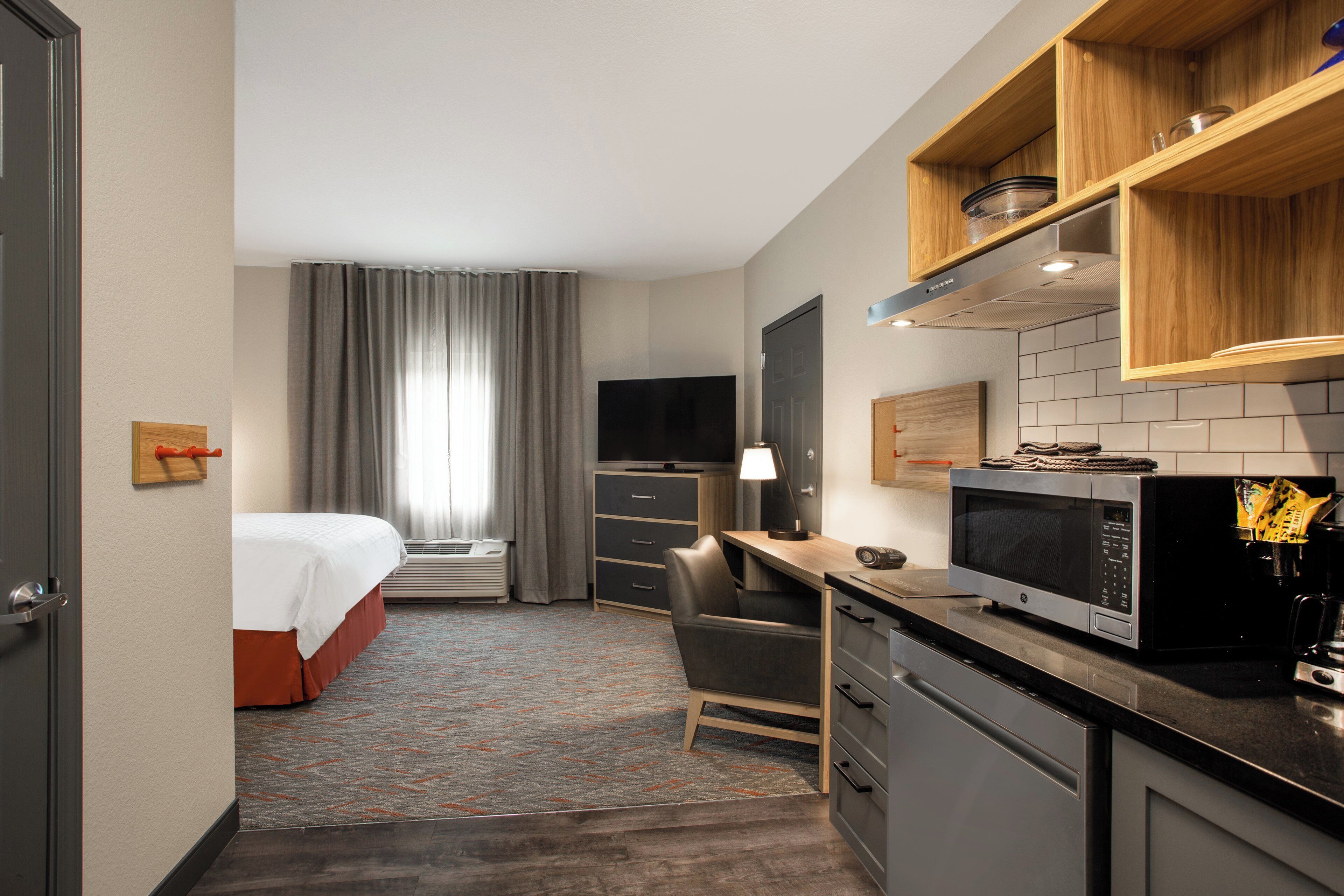 A hotel room with a bed, desk, chair, TV, microwave, and kitchenette.