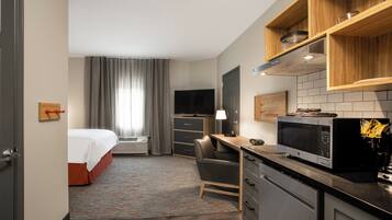 A hotel room with a bed, desk, chair, TV, microwave, and kitchenette.