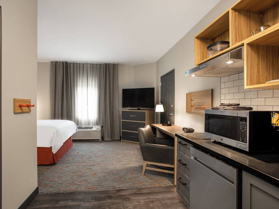 A hotel room with a bed, desk, chair, TV, microwave, and kitchenette.