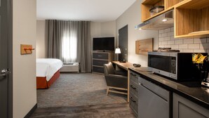 A hotel room with a bed, desk, chair, microwave, and a television.