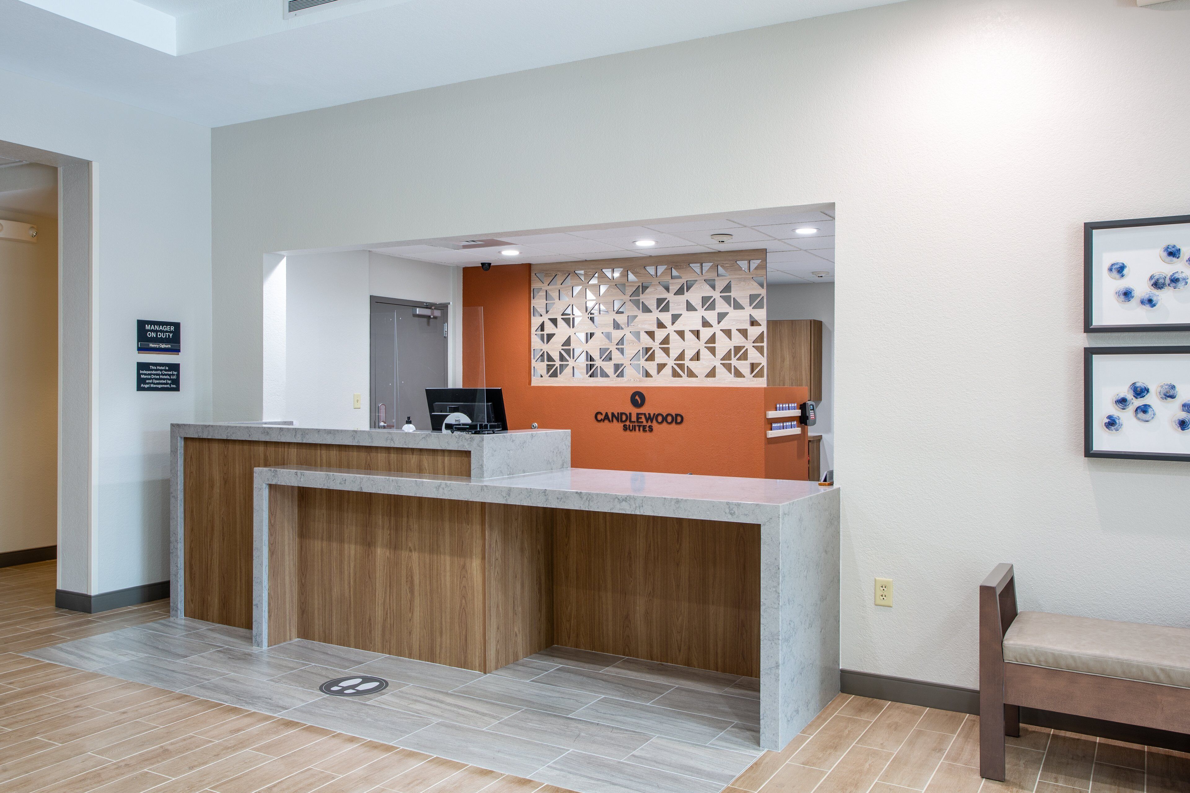 A reception desk with a wooden counter and a modern design. There is a sign above the desk that reads "CANDLEWOOD SUITES."