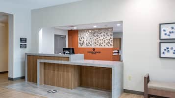 A reception desk with a wooden counter and a modern design. There is a sign above the desk that reads "CANDLEWOOD SUITES."