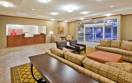 A hotel lobby with a reception desk, seating area, and a large window overlooking the parking area.
