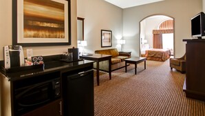 Une chambre d’hôtel équipée d’une kitchenette, d’un canapé, d’une table à manger, d’une télévision et d’un grand tableau encadré au mur.