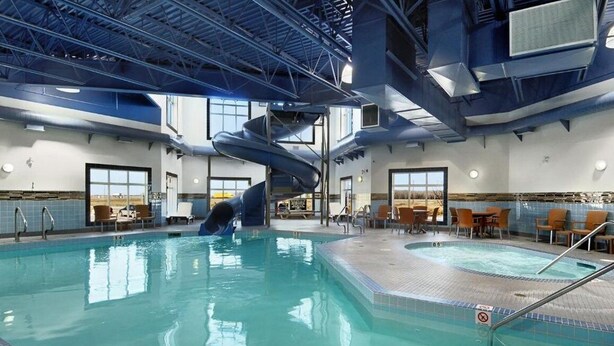 Une piscine intérieure avec un toboggan, des espaces de détente et une vue sur l’extérieur.