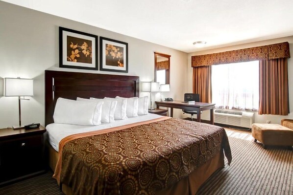A hotel room with a large bed, a desk, a chair, and two framed pictures on the wall.